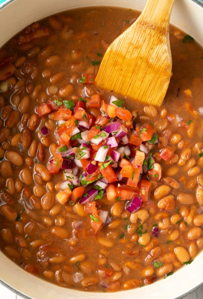 Overhead shot of pinto beans in a large pot with pico de gallo on top.