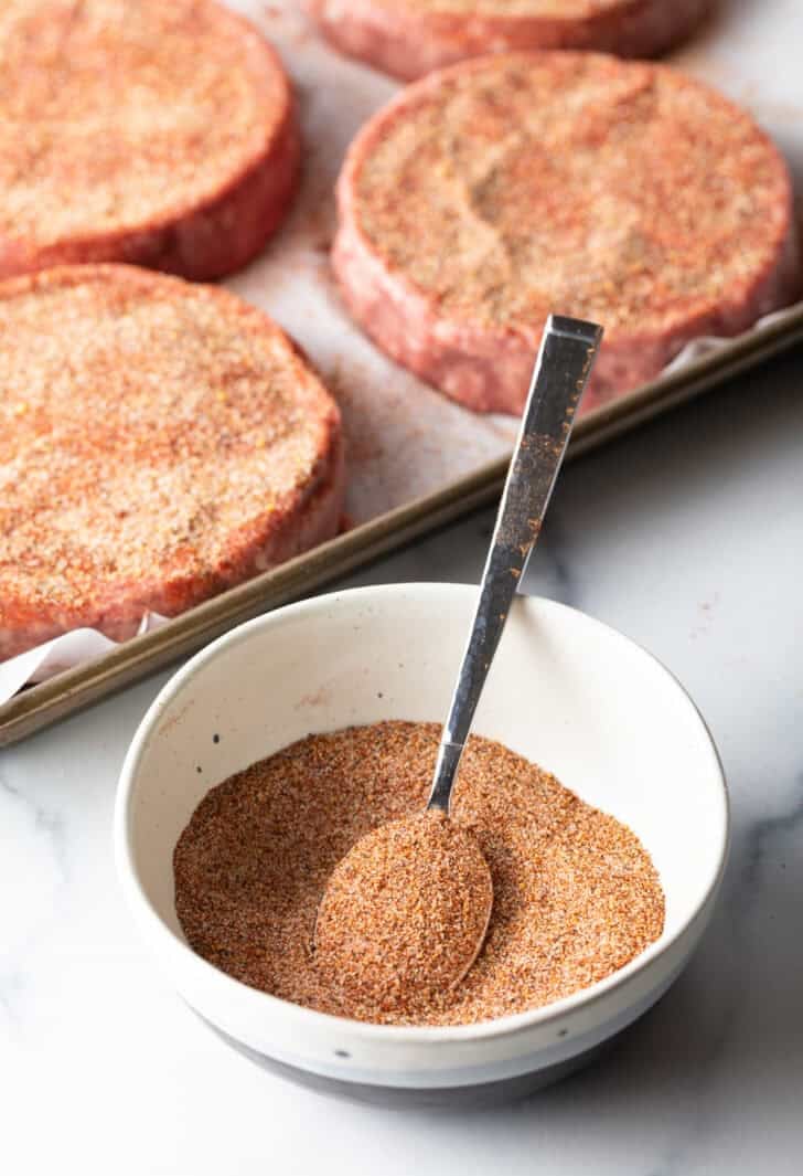 White bowl with mixture of burger seasoning and spoon.