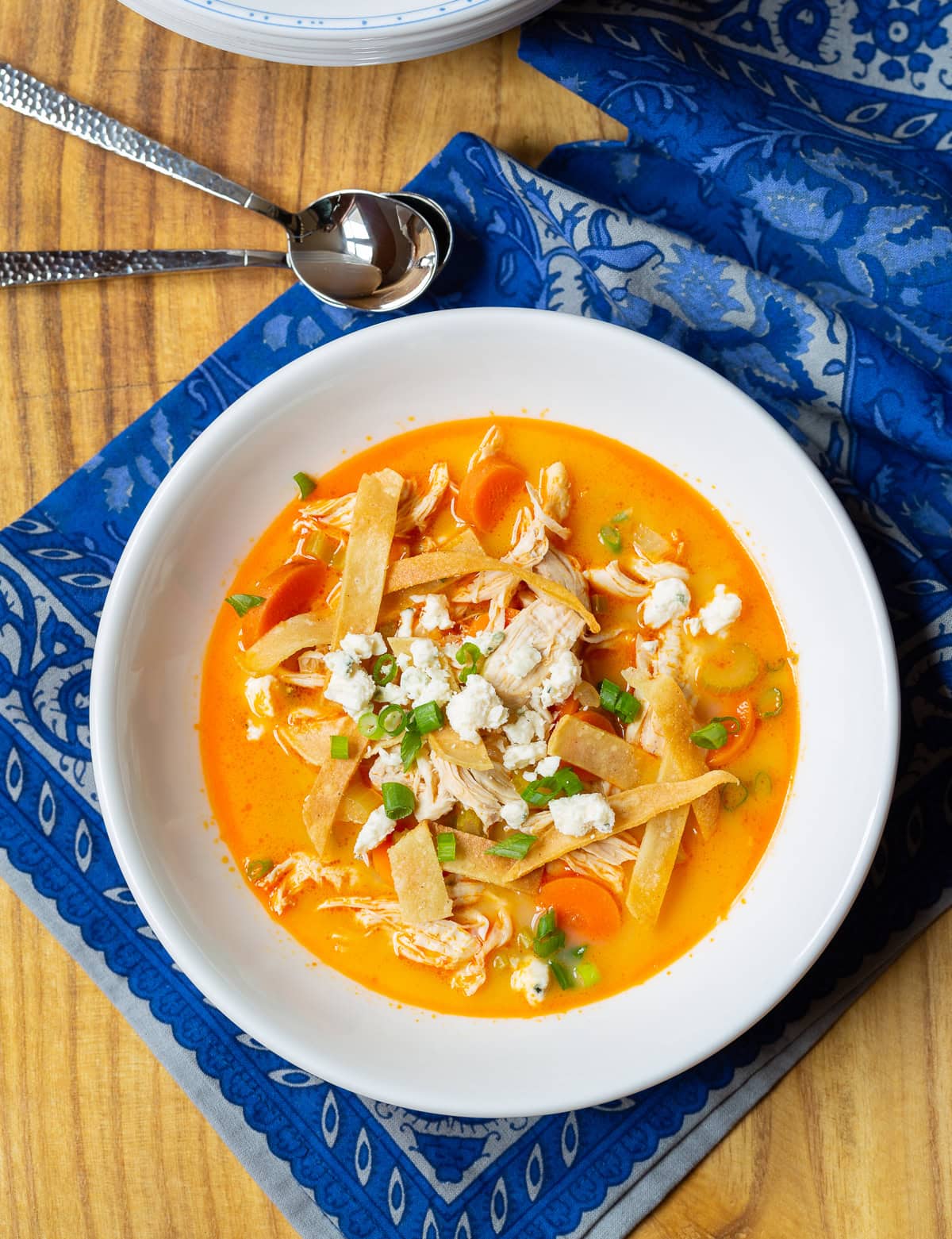 slow-cooker-buffalo-chicken bowl of slow cooker buffalo chicken in a white bowl with a blue cloth underneath.