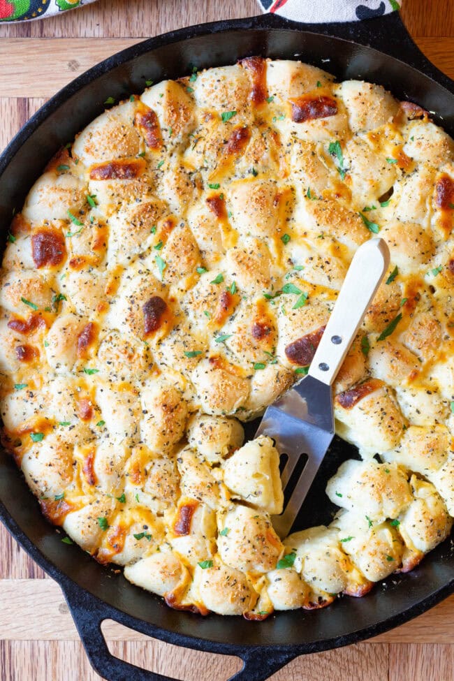 Overhead shot of 6-Ingredient Cheesy Garlic Pull Apart Bread in a skillet with a spatula taking some pieces. 