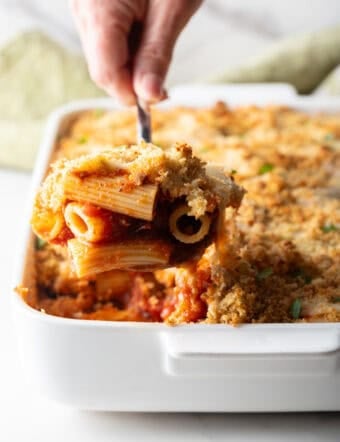 A serving of easy chicken parmesan casserole is being scooped out of a white baking dish.