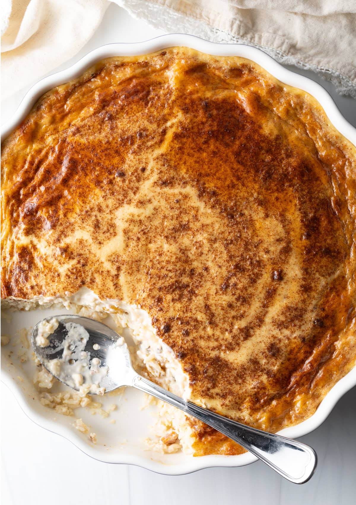 Overhead view of baked rice pudding in a circular dish with a metal spoon where a portion has been removed.