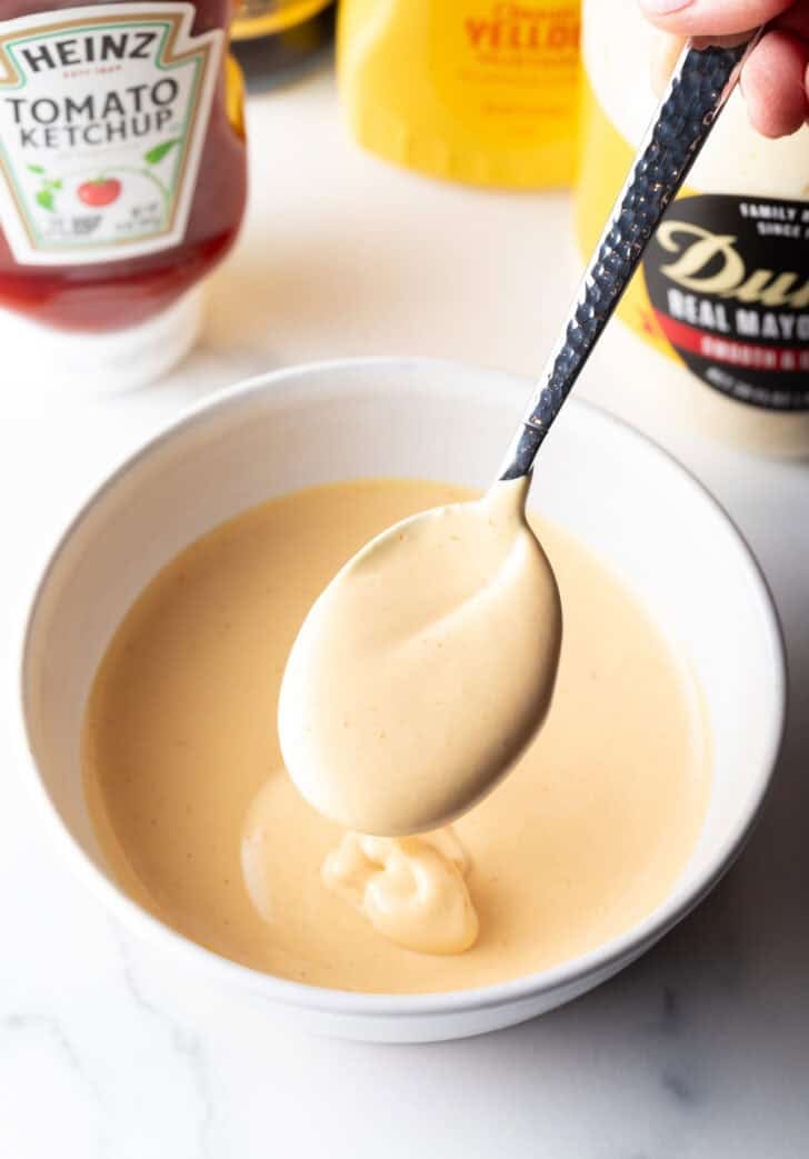 Spoon of burger sauce held over a bowl of sauce.