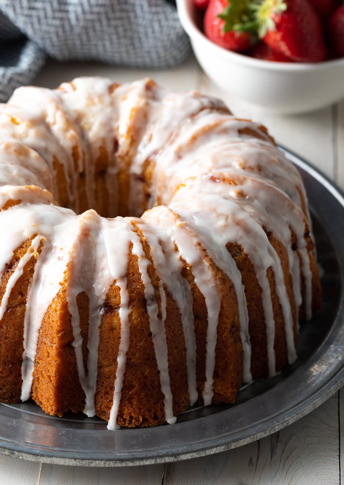 Strawberry bundt cake with lemon glaze on a silver serving platter. 