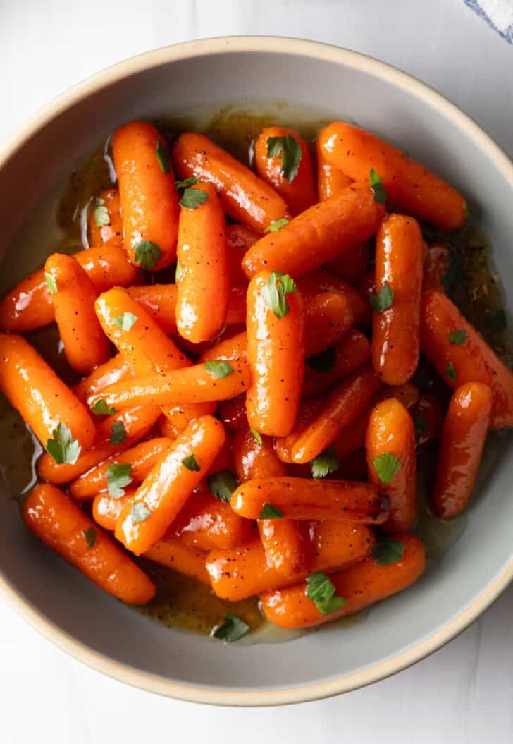 Top down bowl of glazed honey baby carrots sprinkled with chopped parsley.