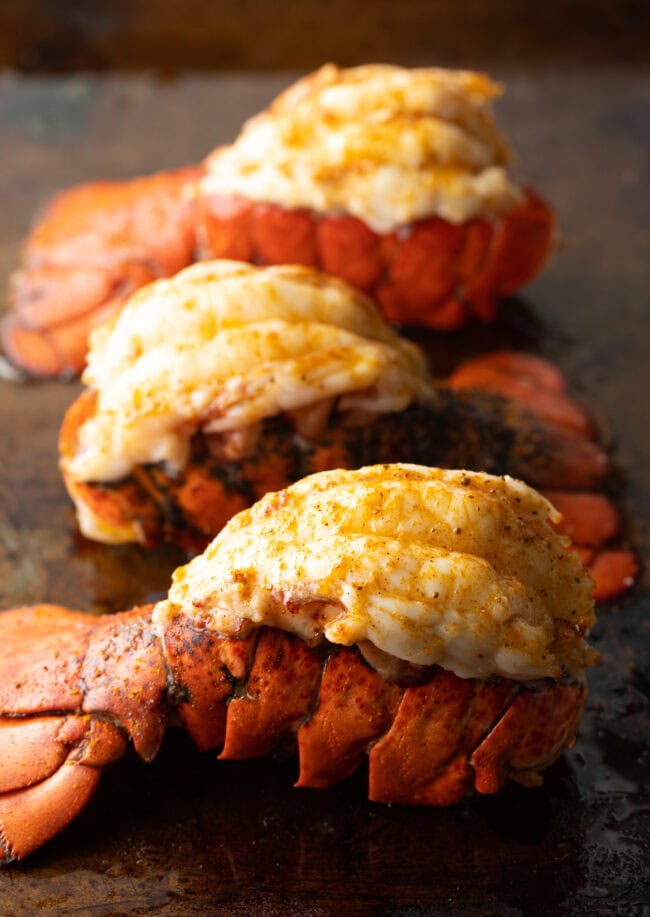 Three plump cooked lobster tails on a baking sheet.