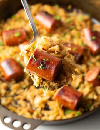 Close view of a piece of cooked sausage on a spoon with sauerkraut.