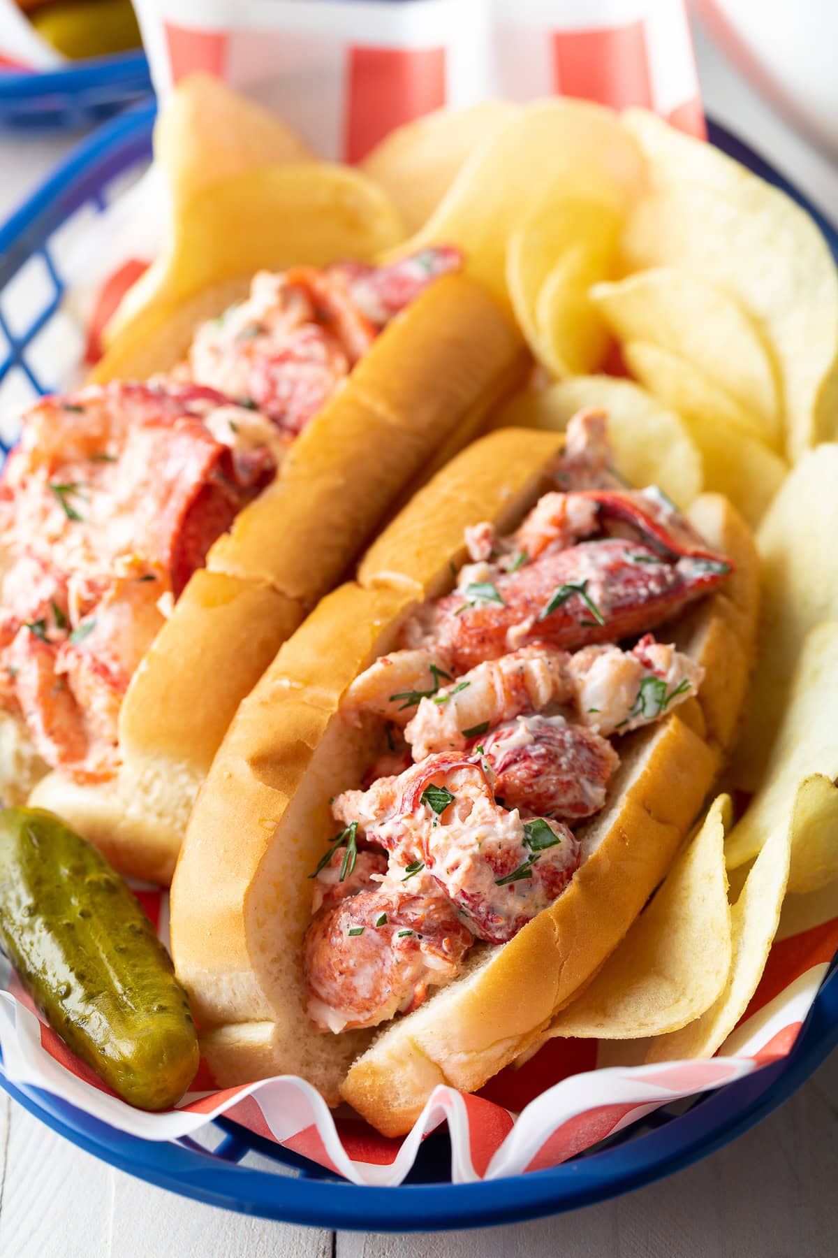 Two lobster rolls in a basket with chips and a pickle. 