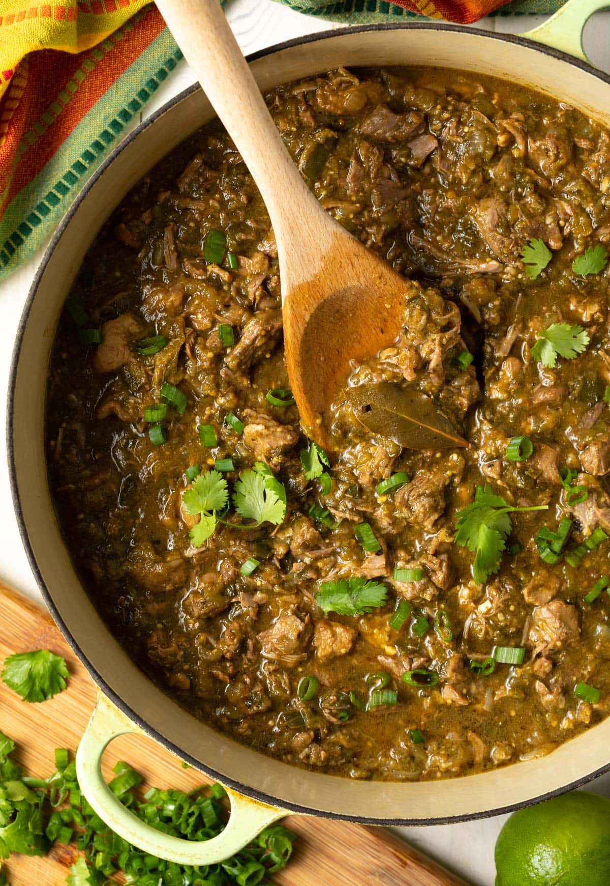Dutch oven full of pork green chili recipe with a wooden spoon. 