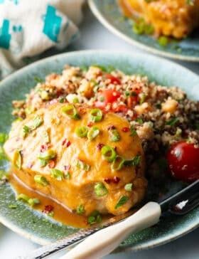 Baked pork chop covered with glaze and chopped scallions, on a plate next to quinoa salad with tomatoes.