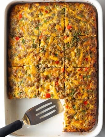 Pan of egg casserole with sausage and vegges. A spatula is in the pan, with square portions of the casserole removed.