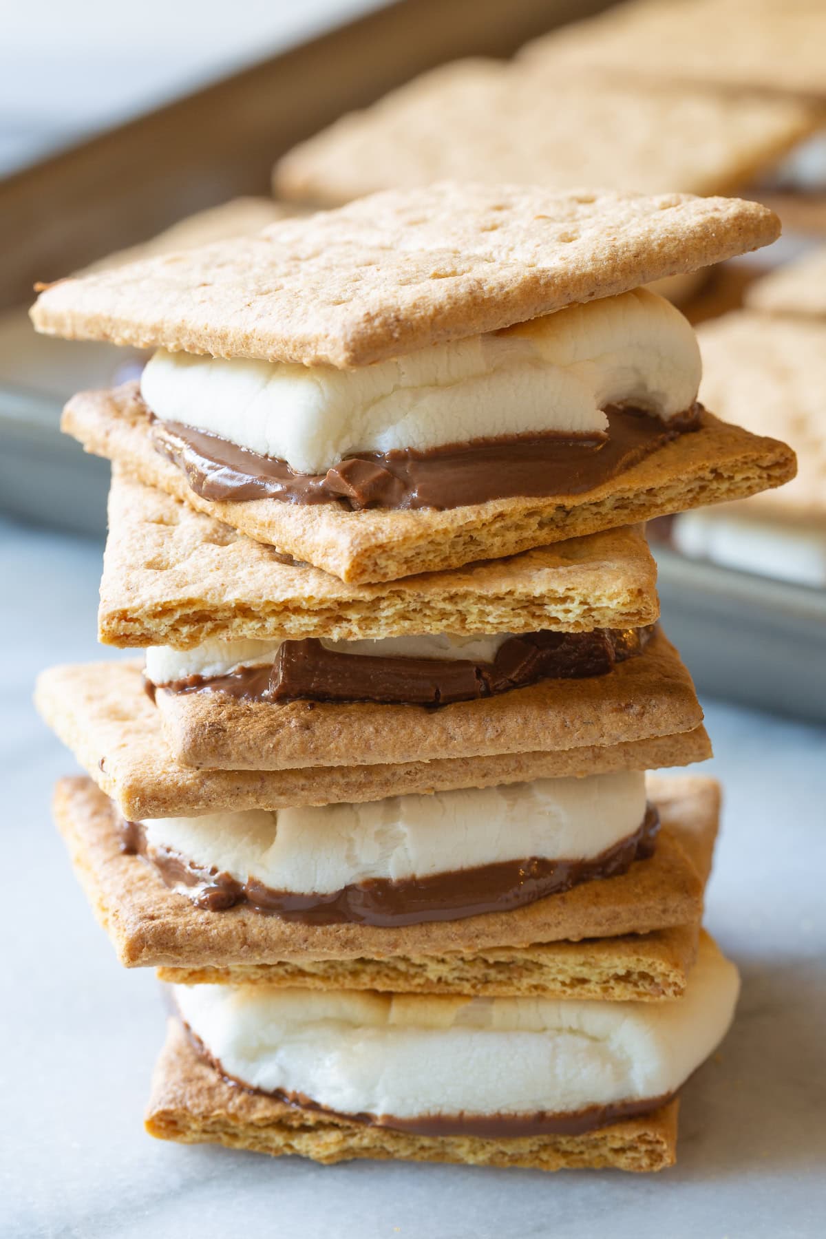 How To Make Smores In The Oven -Baked s'mores sandwiches stacked on top of each other.