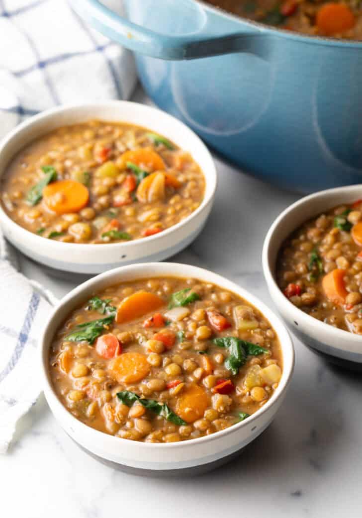 3 white bowls of lentil soup with carrots and kale.