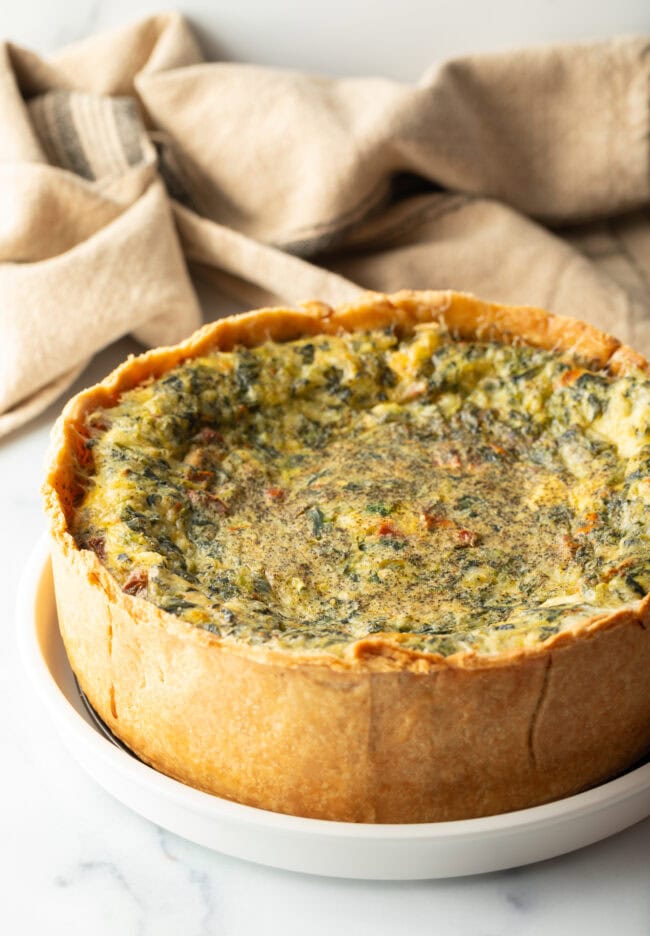 Baked veggie quiche with a deep dish crush on a white round plate.